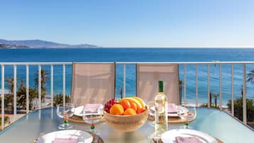 Mesa para dos con frutero, botella de vino y copas, con vista al océano.