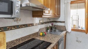 Eine kompakte Küche mit eingebauter Mikrowelle, einer Edelstahl-Dunstabzugshaube, einer Granitabdeckung, einem Spülbecken und Holzschränken.