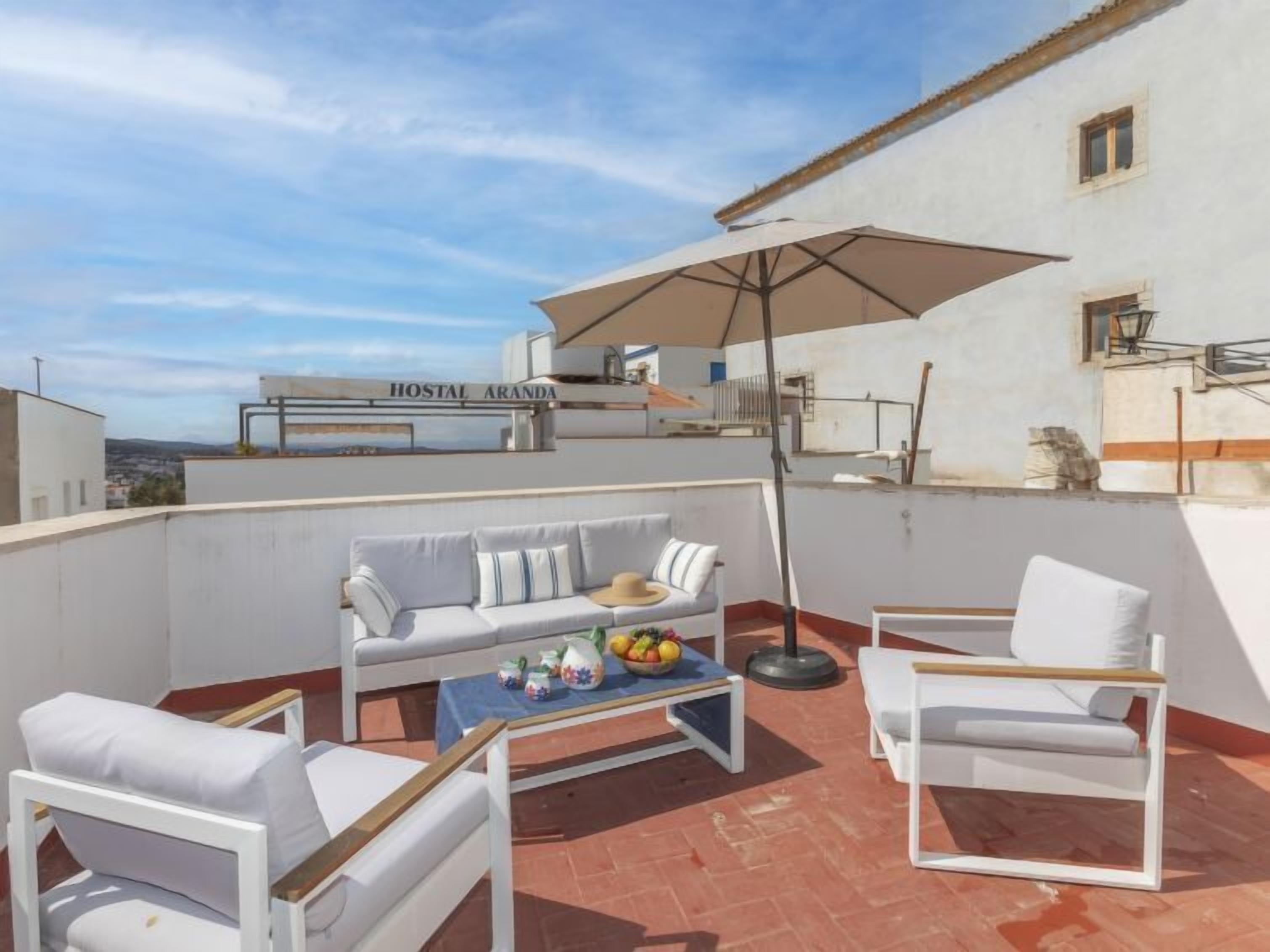 A rooftop terrace with a white sofa, two white armchairs, a coffee table, and a large umbrella.