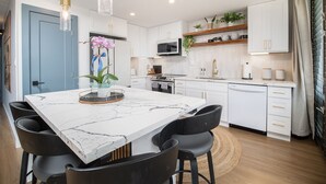 A modern kitchen with white cabinetry, a marble countertop, and black chairs. - Maui Parkshore 204 2BR across Kamaole III Beach w/ ocean views, summer deal (Kihei)