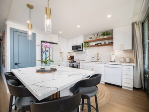 A modern kitchen with white cabinetry, a marble countertop, and black chairs.