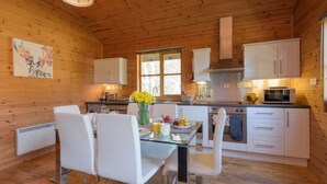 A wooden cabin interior with a dining area, kitchen, and a large window. - Cosy, comfortable lodge sleeps 6 guests  in 3 bedrooms. Pet friendly! (Banchory)