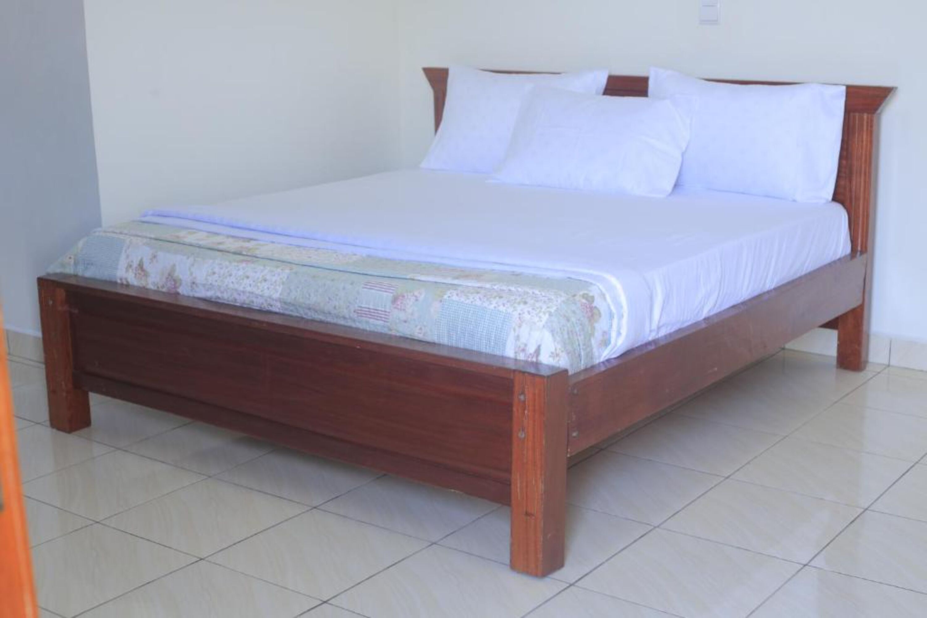 A single bed with a wooden frame and white bedding in a room with tiled flooring.