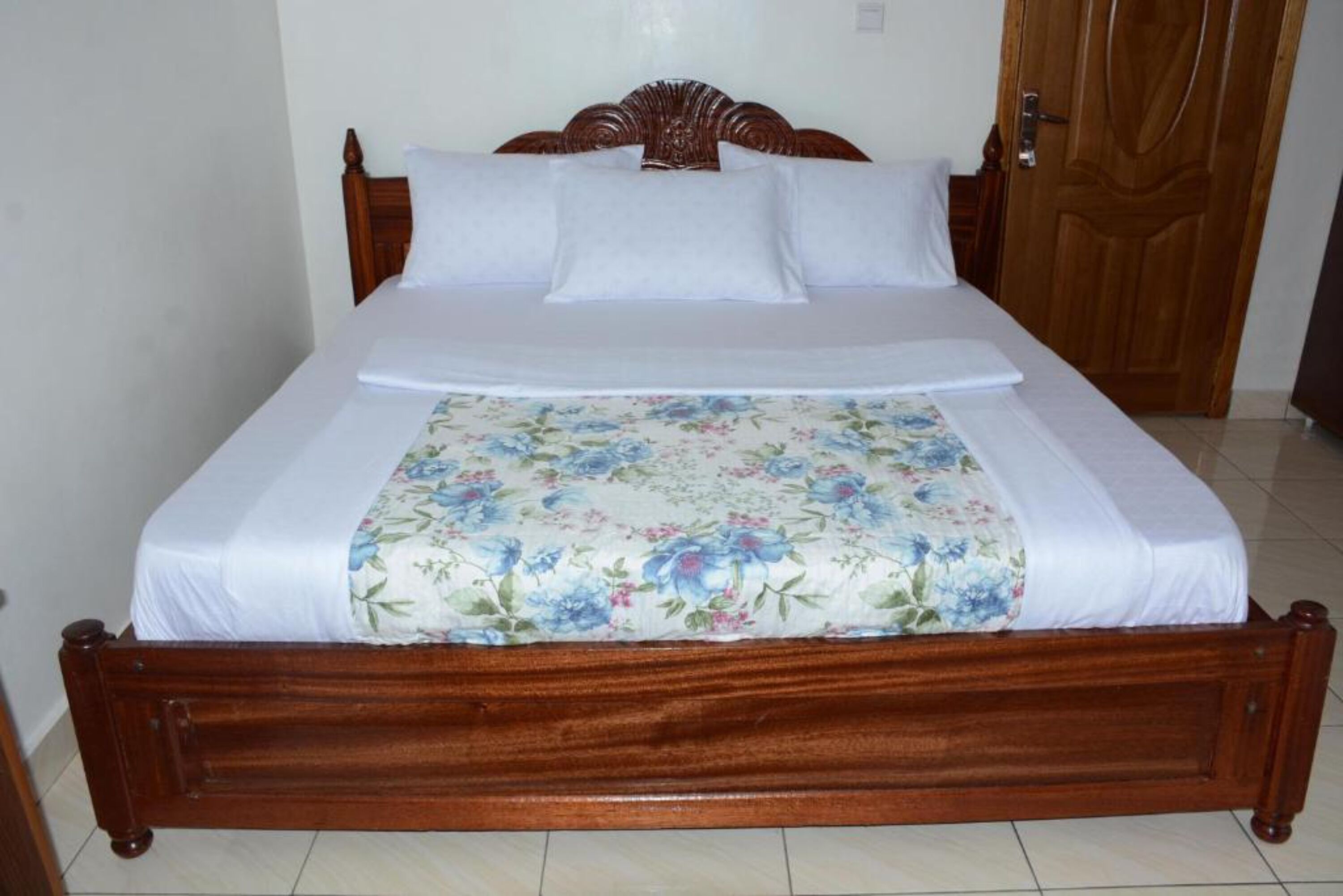A wooden bed with white bedding and a floral-patterned blanket.