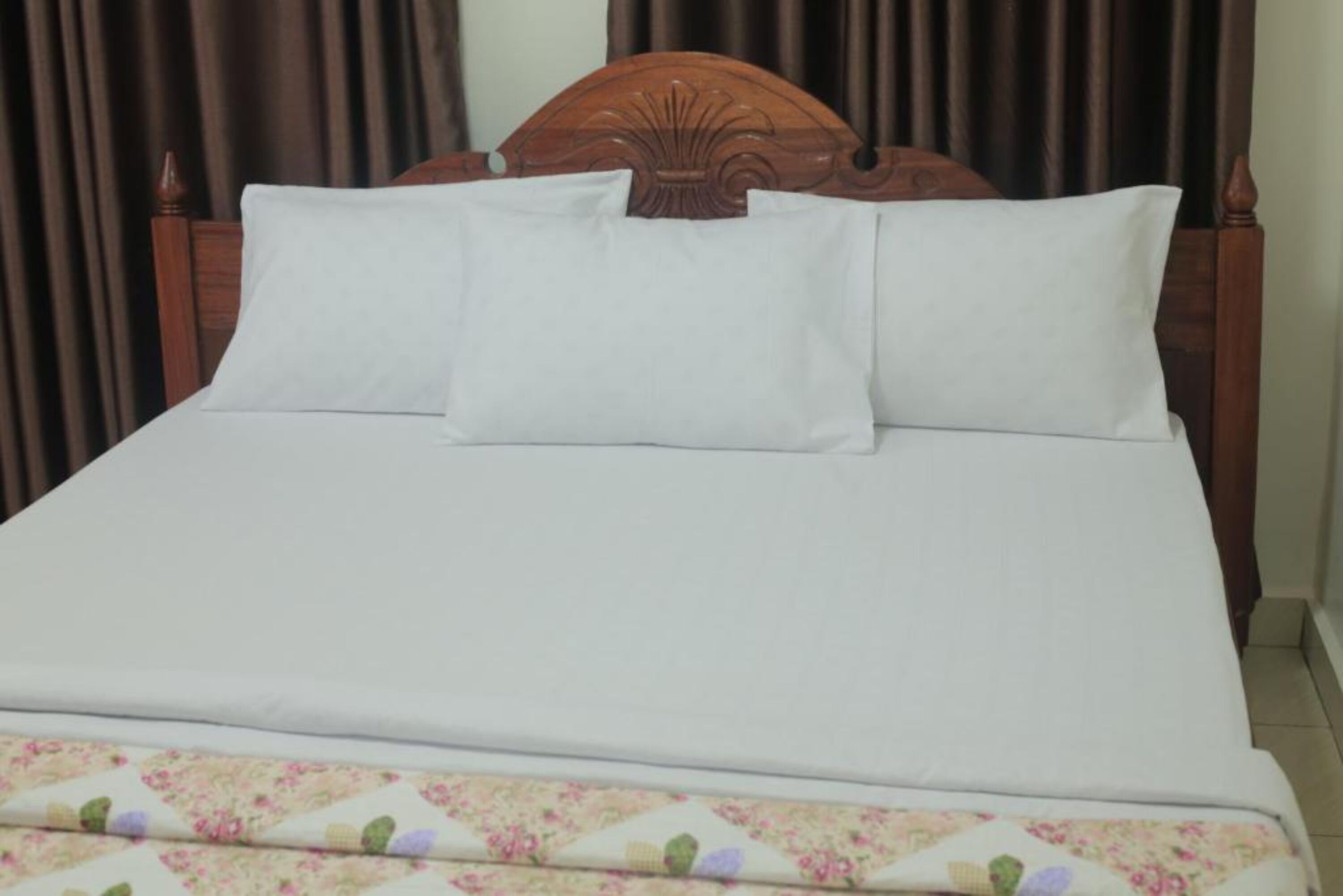 Ein Bett mit Holz-Kopfteil, weißer Bettwäsche und einer Decke mit Blumenmuster.