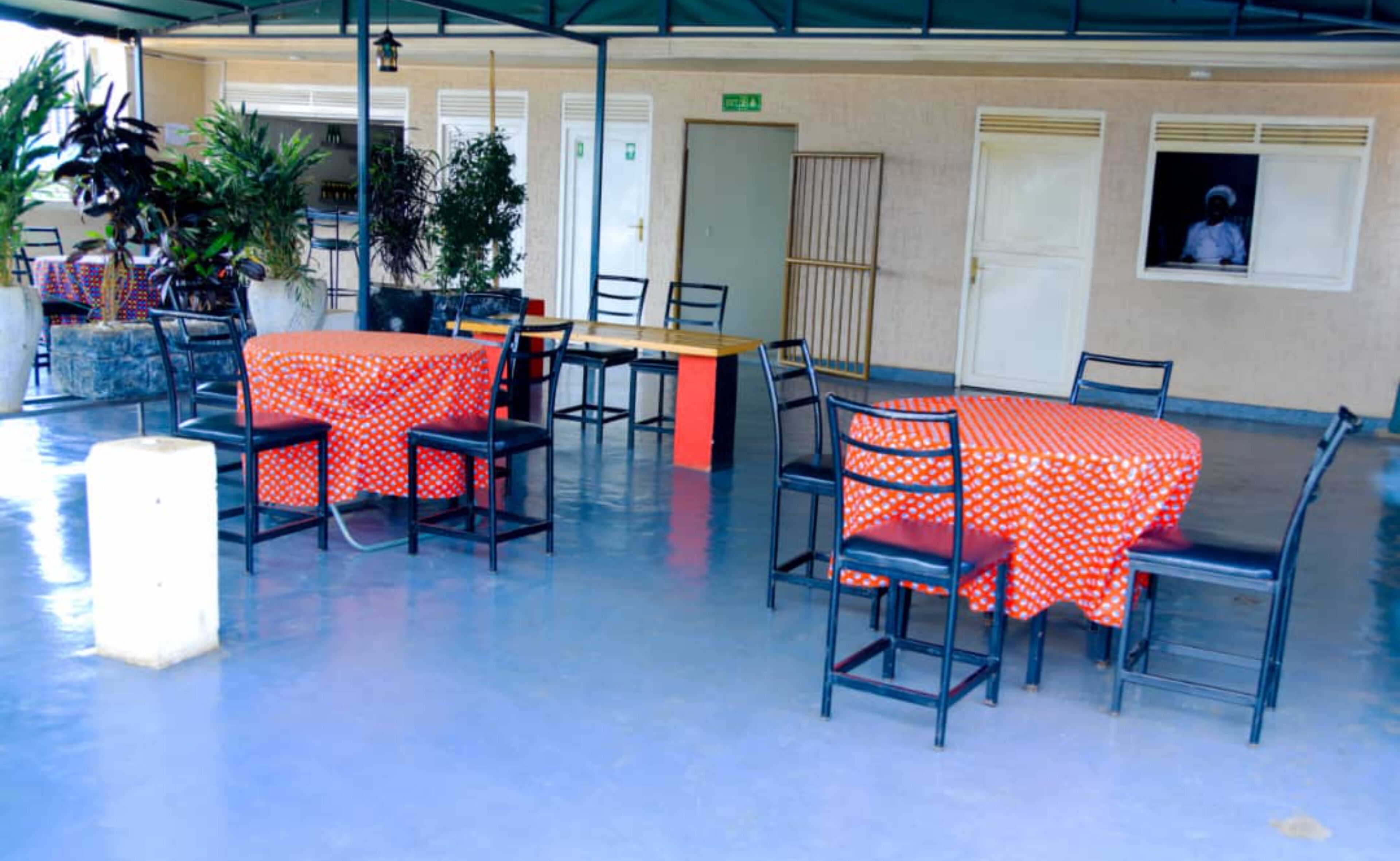 An outdoor patio area with tables and chairs, some covered with red polka dot tablecloths, and potted plants.