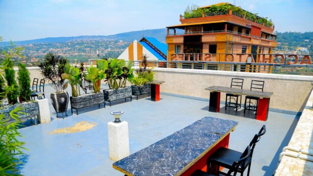 Una terraza en la azotea con una mesa y sillas de mármol, rodeada de plantas en macetas y vistas a un horizonte urbano distante.