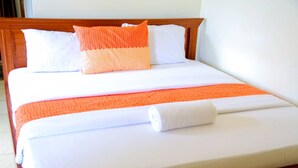 Una cama bien tendida con ropa de cama blanca y naranja, un cabecero de madera y una almohada blanca.