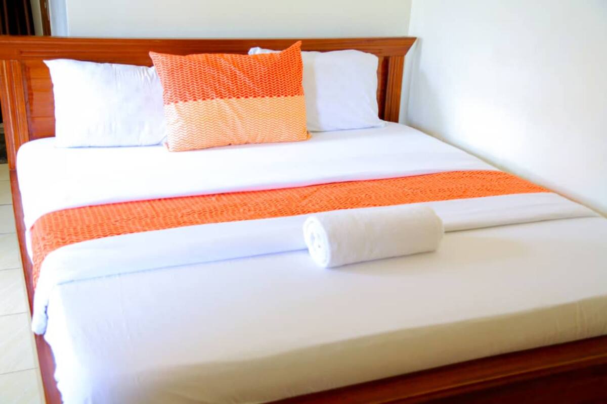 A neatly made bed with white and orange bedding, a wooden headboard, and a white pillow.