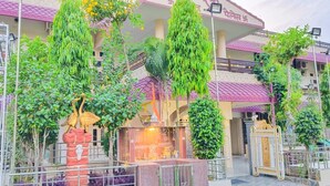 A courtyard with a shrine, surrounded by greenery and a building with a purple roof. - Hotel Prabhat Palace (Kota)