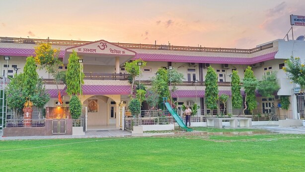 A hotel with a prominent entrance, a covered area with a statue, and a playground with a slide. - Hotel Prabhat Palace (Kota)