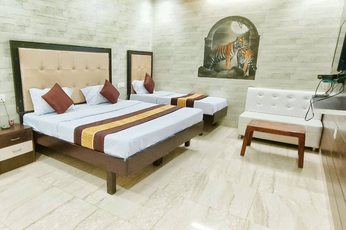 Habitación de hotel con dos camas, un escritorio pequeño, un espejo, un televisor y una obra de arte colgada en la pared que representa un tigre.