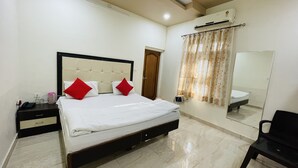 A hotel room with a bed, bedside table, mirror, and an air conditioning unit. - Hotel Prabhat Palace (Kota)