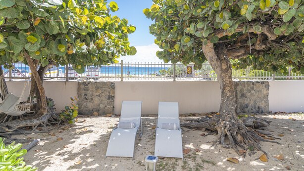 A beachside lounge area with two white sun loungers, a hammock, and a stone wall. - Condo on the beach (Collectivité de Saint-Martin)
