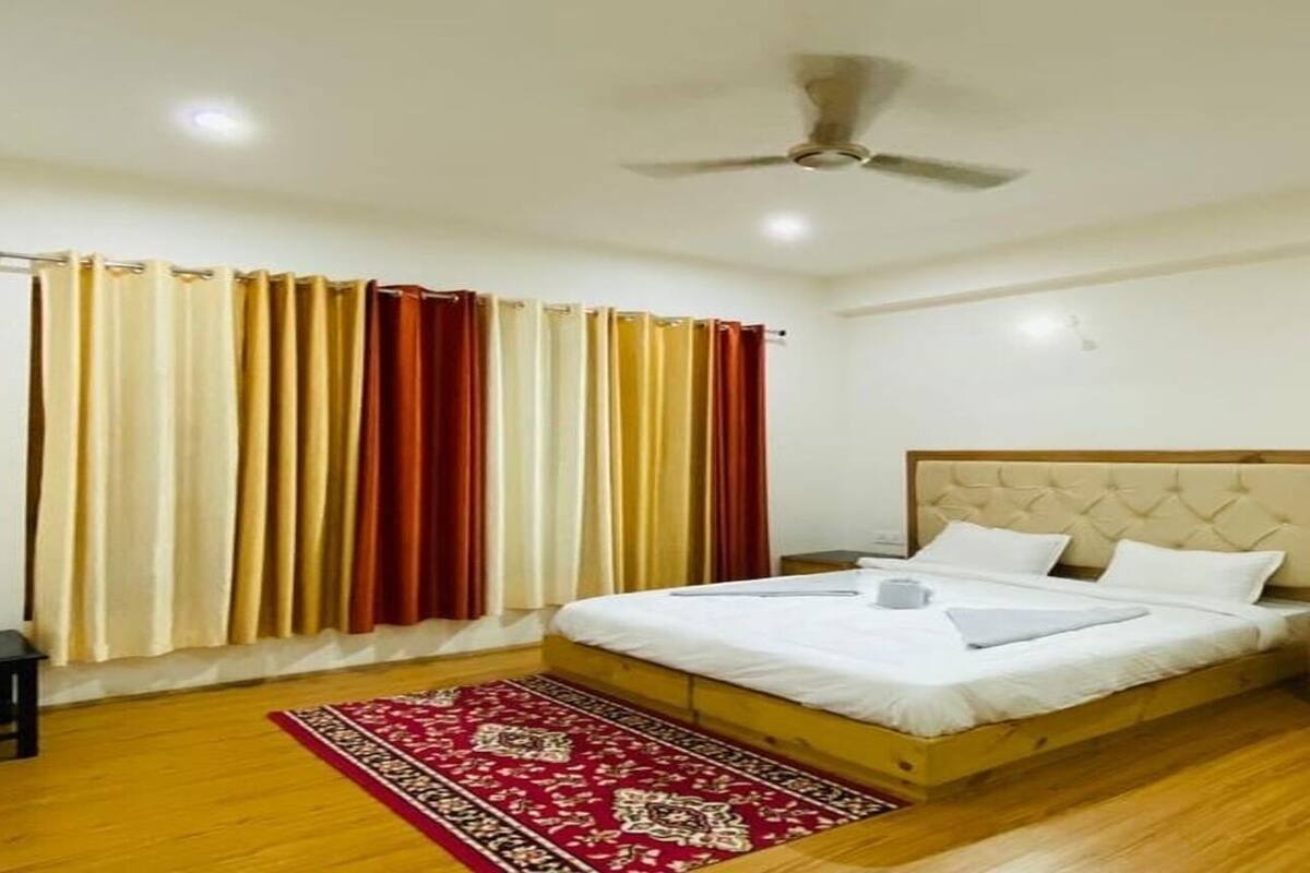 A bedroom with a bed, a ceiling fan, a red patterned rug, and curtains.