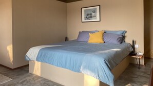 Une chambre à coucher avec un lit, une table de chevet, un tableau encadré au mur et un appareil de climatisation.