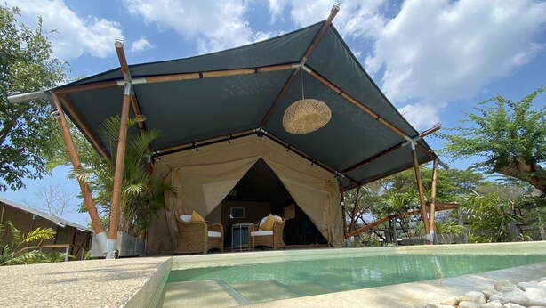 Un espace extérieur aménagé avec une tente, doté d’une piscine, et entouré de rochers et de palmiers.