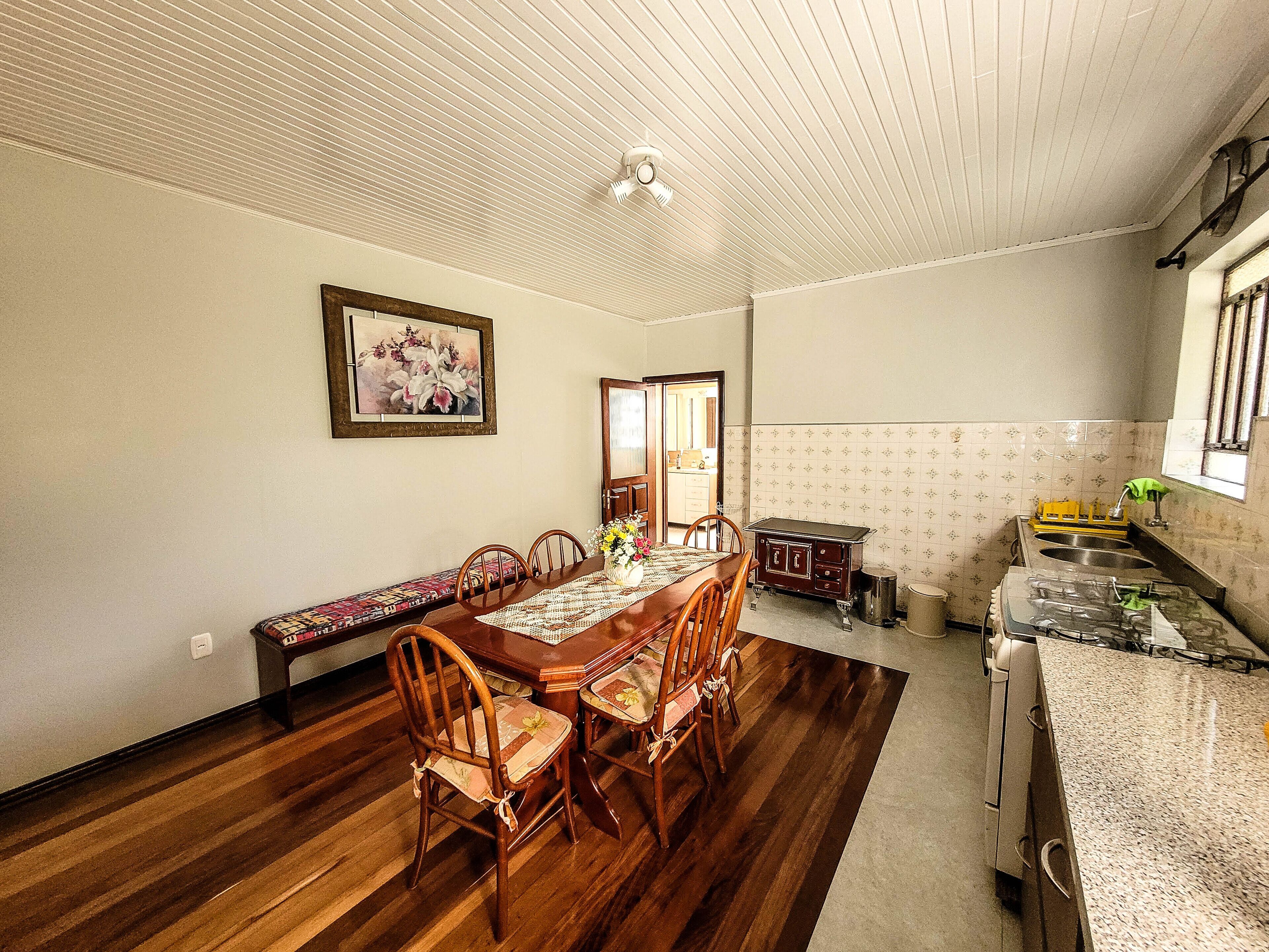 A dining area with a wooden table and chairs, a bench, a kitchen with a sink and stove, and a ceiling fan.