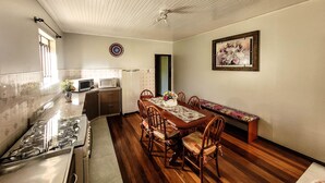 Uma cozinha com fogão, micro-ondas, frigorífico e mesa de jantar de madeira com cadeiras.