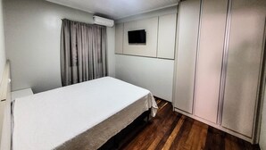 Quarto com cama, guarda-roupa, televisão e ar condicionado.