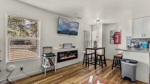 A modern kitchen with a fireplace, wooden flooring, white cabinets, and a kitchen island. - Beaver Street Chalet w/AC, Fully Fenced Yard, 3 Smart TVs, W/D, and Speedy Wi-Fi (Flagstaff)