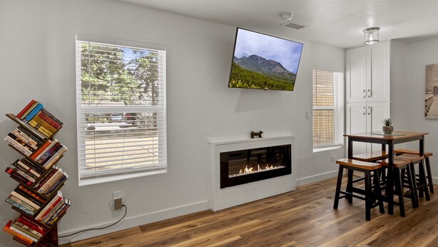 A living room with a fireplace, bookshelves, a TV, and a dining area. - Beaver Street Chalet w/AC, Fully Fenced Yard, 3 Smart TVs, W/D, and Speedy Wi-Fi (Flagstaff)