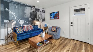 A living room with a blue sofa, a patterned armchair, a wooden coffee table, and a large wall mural. - Beaver Street Chalet w/AC, Fully Fenced Yard, 3 Smart TVs, W/D, and Speedy Wi-Fi (Flagstaff)