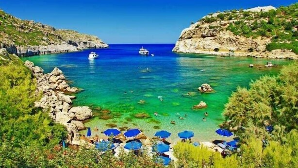 Paesaggio costiero con acque turchesi cristalline, scogliere rocciose e una barca all'orizzonte.