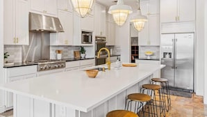 A modern kitchen with white cabinetry, stainless steel appliances, and pendant lighting. - Beachfront Villa | Concierge Services (Kingsland)
