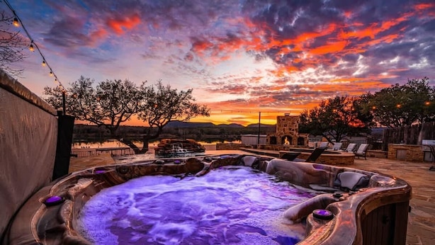A hot tub with a stone structure in the background, surrounded by outdoor seating and a sunset view. - Beachfront Villa | Concierge Services (Kingsland)