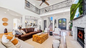 A spacious living area with a fireplace, a high ceiling, and a staircase leading to an upper level. - Beachfront Villa | Concierge Services (Kingsland)