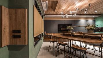A modern kitchen with wooden cabinetry, a long dining table, bar stools, and a hanging light fixture.