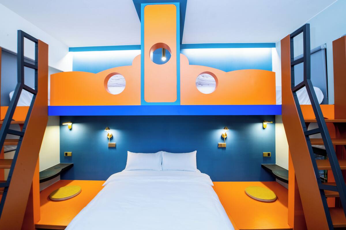 A bunk bed room with orange and blue walls, a ladder on each side, and a central circular window.