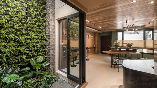 Een moderne keuken met een glazen deur naar een eetgedeelte, een houten plafond en een groene wand met planten.