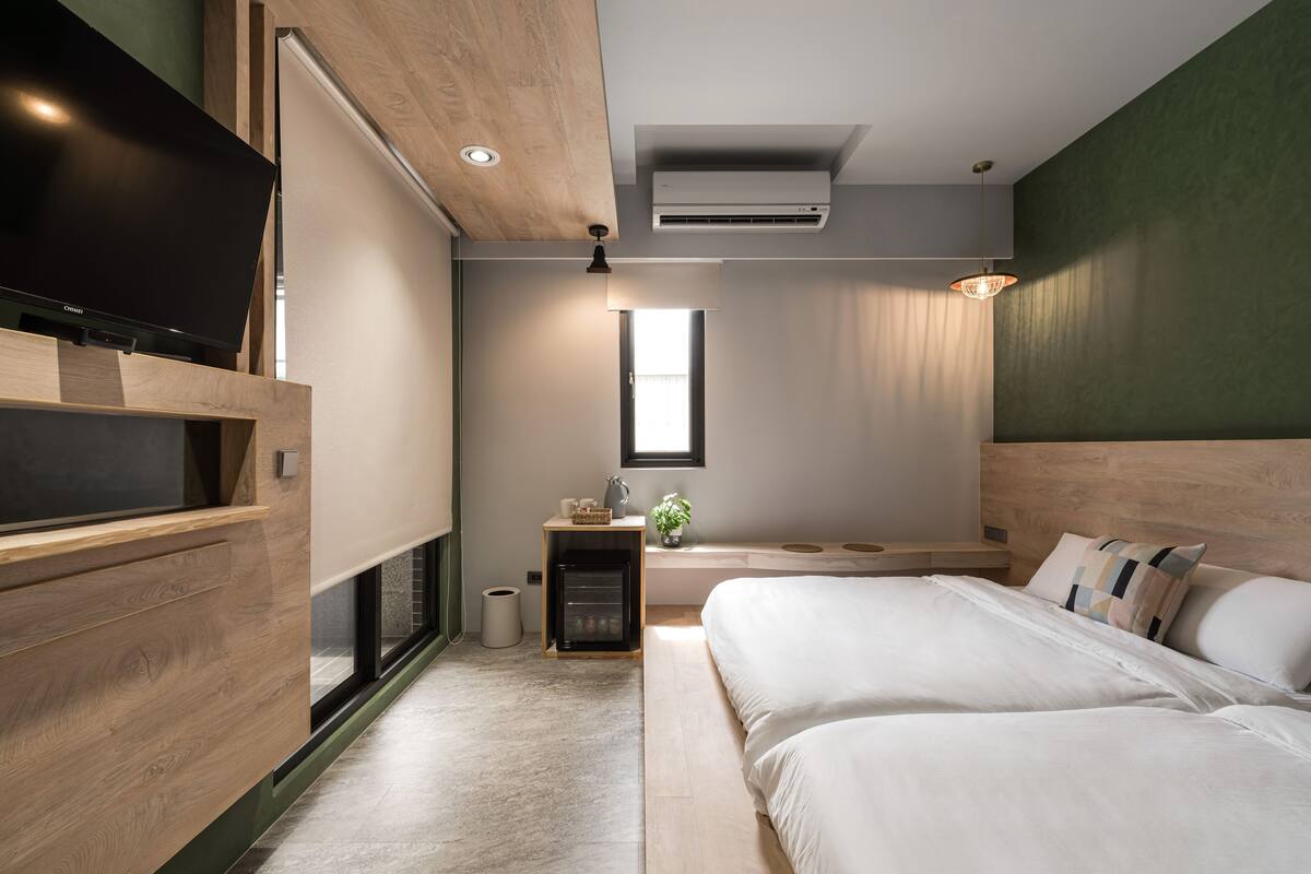 A modern bedroom with a large bed, a TV, and a small seating area with a plant.