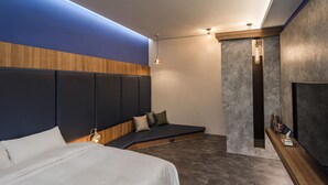 Een moderne hotelkamer met een groot bed, een ingebouwde bank, een televisie en een klein plankje met spullen.