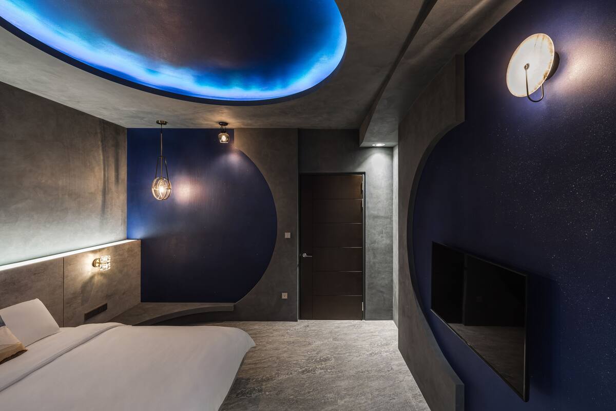 A modern bedroom with a curved ceiling, a bed, a wall-mounted TV, and a door.