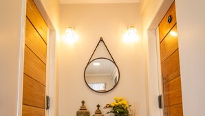 Um corredor com portas de madeira, um espelho, um aparador de madeira com objetos decorativos e um tapete de entrada.