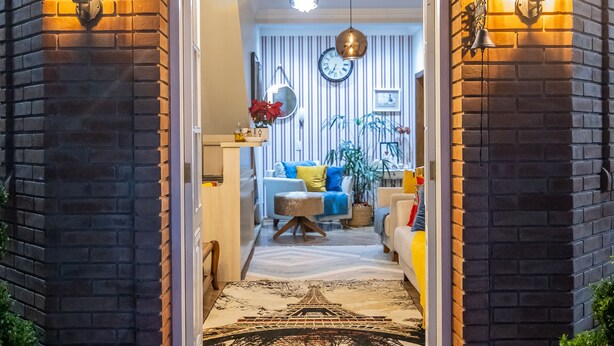 Uma entrada de tijolos com um arco acolhedor que dá acesso a uma sala de estar com sofá, mesa de centro e plantas decorativas.
