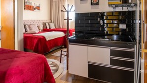 Quarto compacto com cozinha compacta, duas camas com roupa de cama vermelha, teto de madeira e parede branca com um quadro emoldurado.