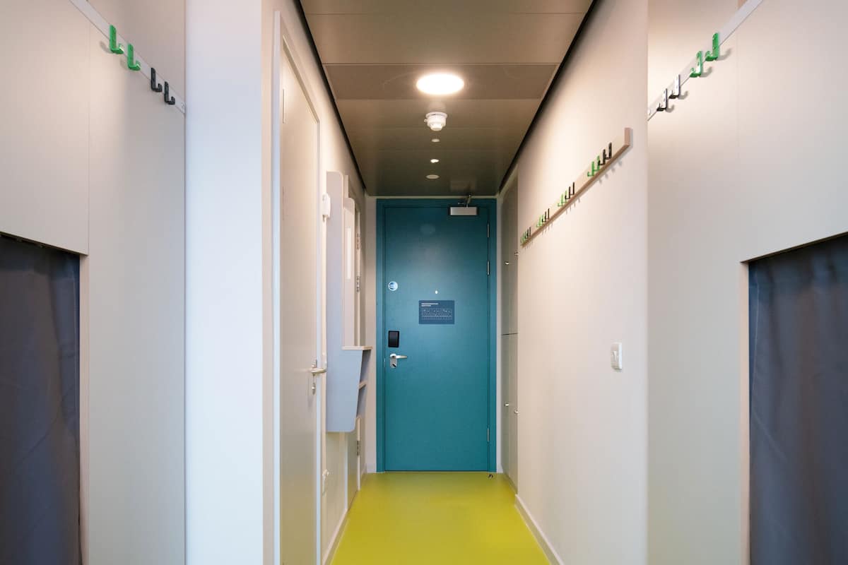 A hotel hallway with a green carpet, white walls, and a blue door at the end.