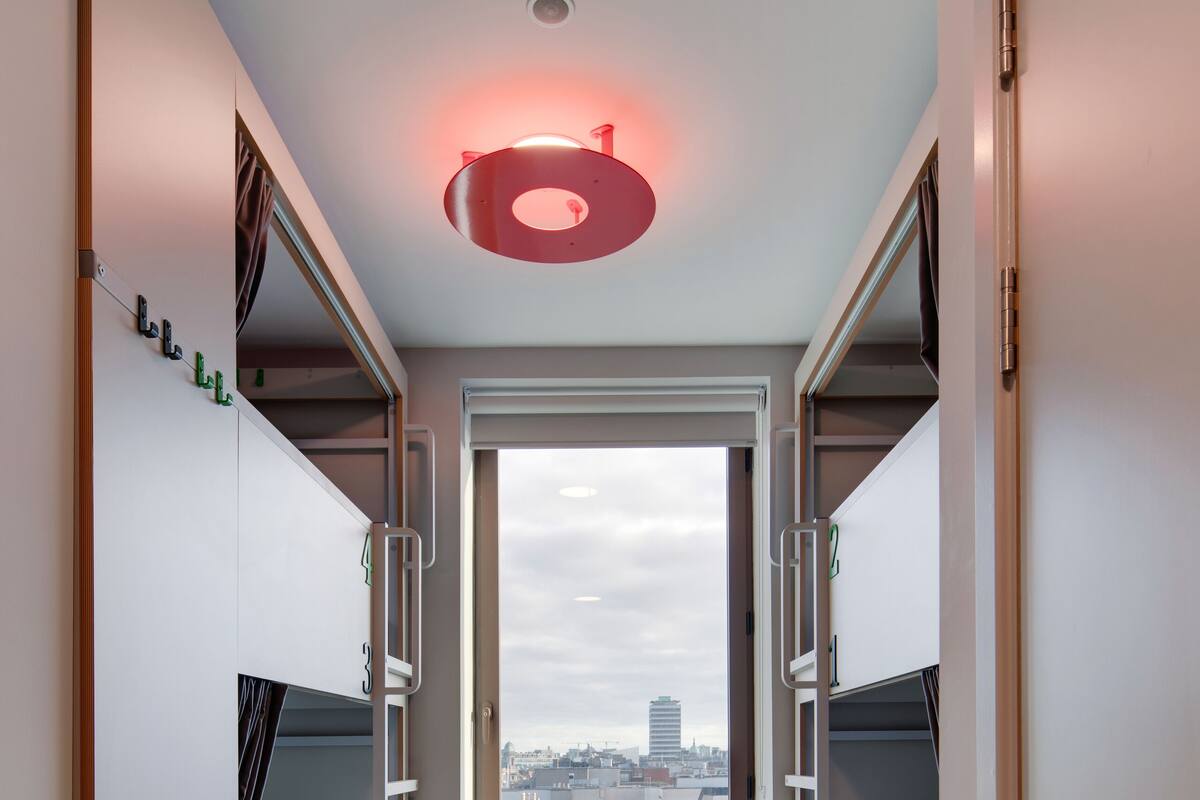 A compact room with bunk beds, a window with a city view, and a circular light fixture on the ceiling.