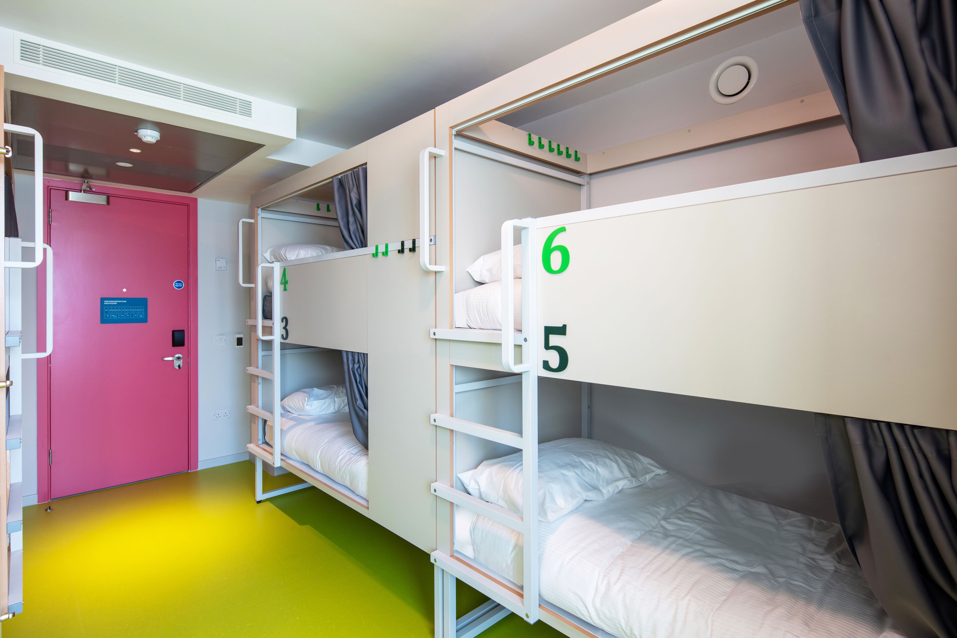 A room with bunk beds numbered 4, 5, and 6, a pink door, and a green floor.
