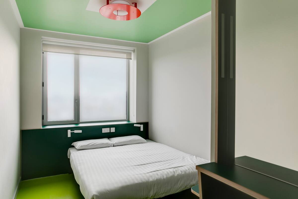 A bedroom with a bed, a window, and a green wall.