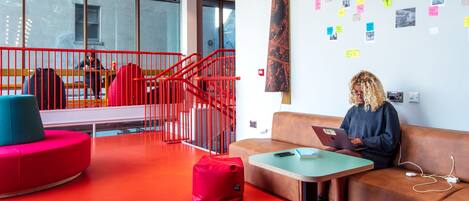 Un interior moderno con asientos rojos, una escalera y una pared con fotografías y notas.