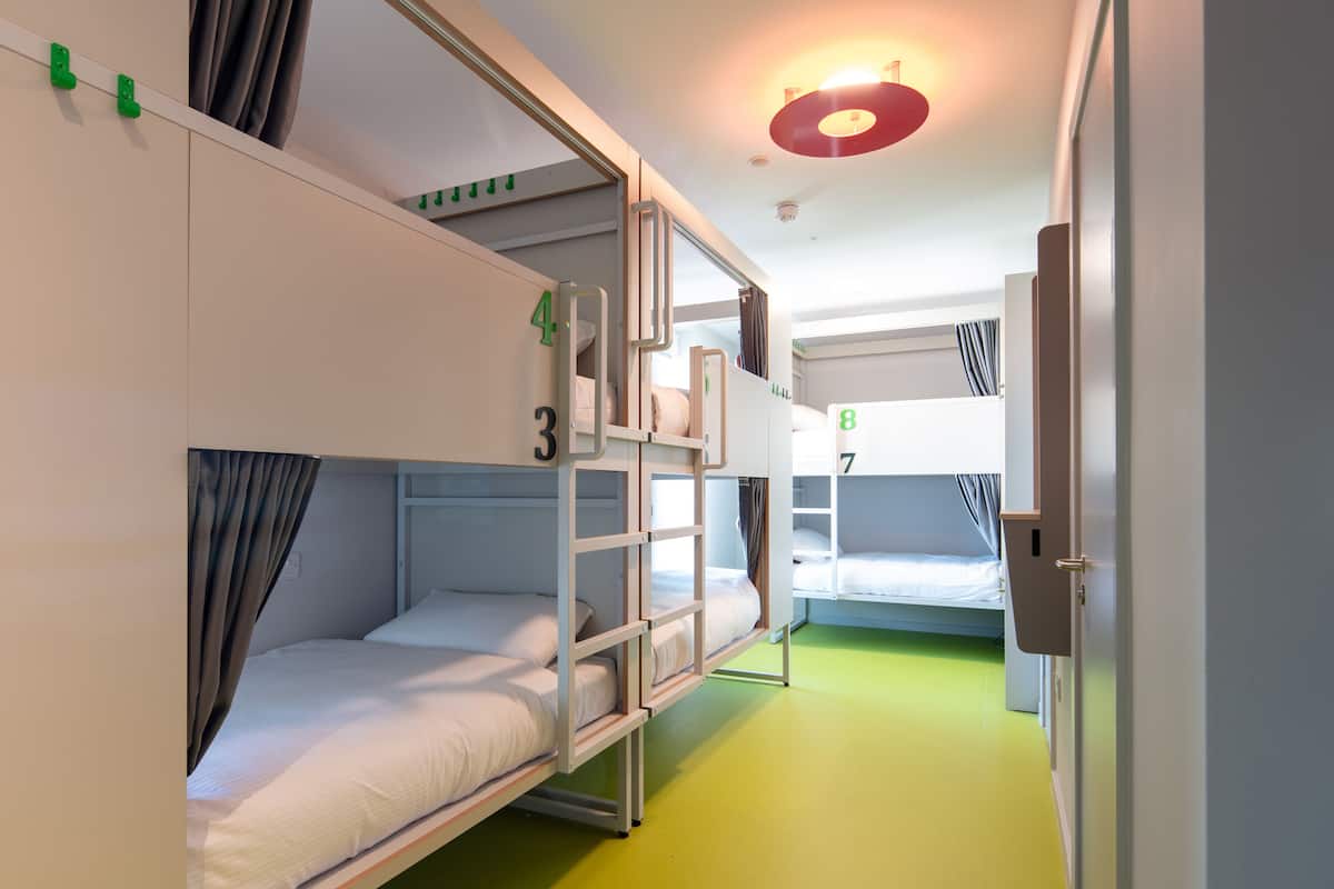 A dormitory room with bunk beds, numbered beds, and a green floor.