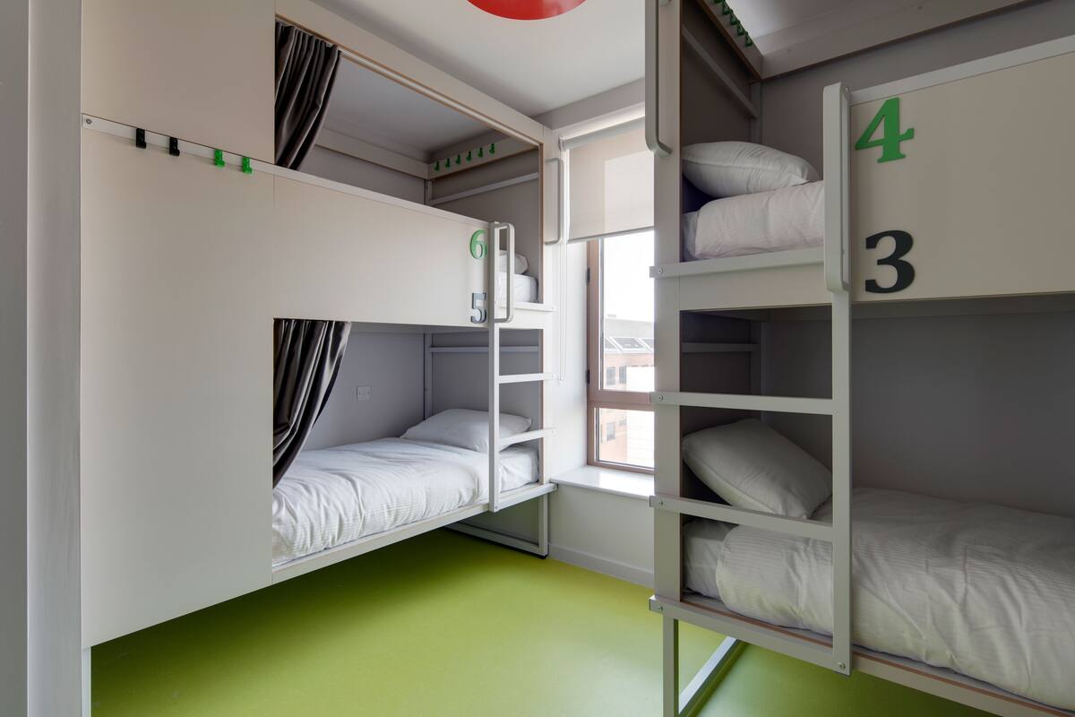 A dormitory room with bunk beds, a window, and a green floor.
