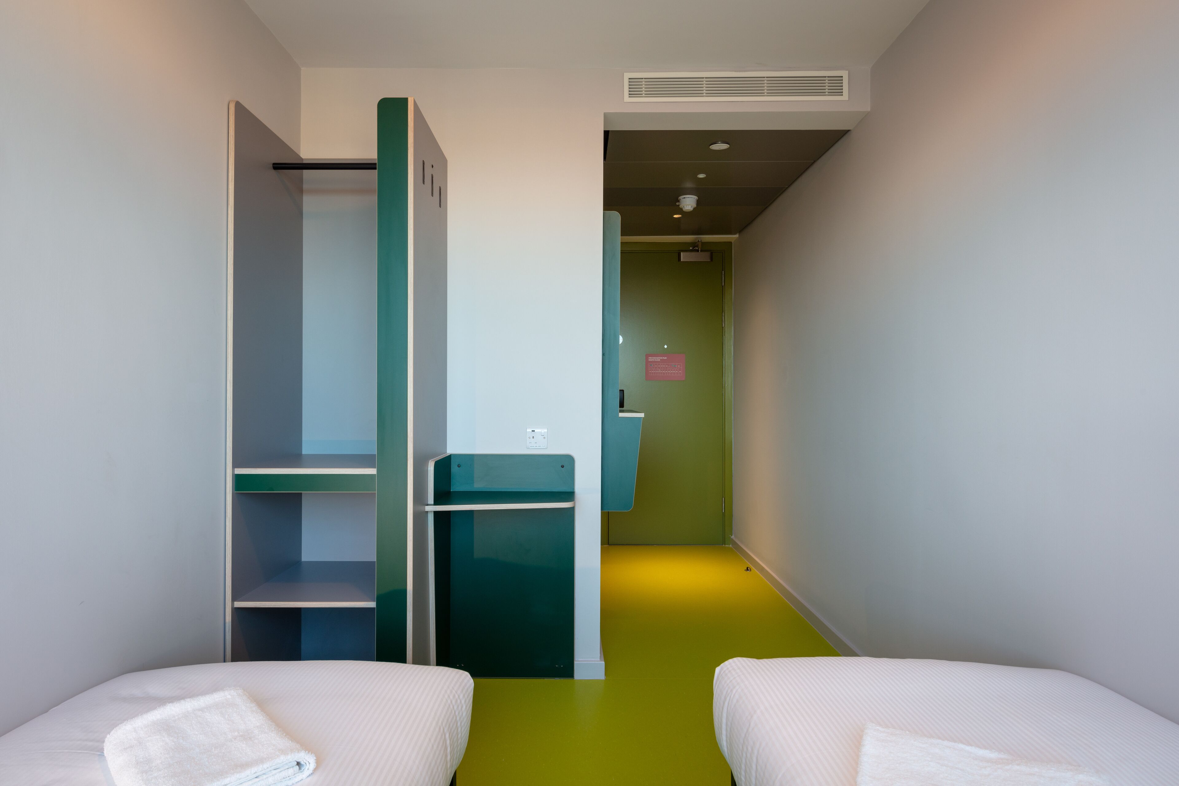 A room with two beds, a green floor, and a closet with a mirror.