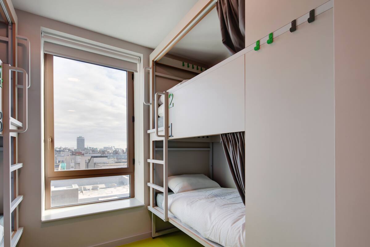 A bunk bed room with a window, a ladder, and a city view.