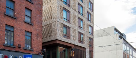 Un edificio de varios pisos con una combinación de fachadas de ladrillo y vidrio moderno, con un letrero de restaurante visible y una línea de tranvía que transcurre frente al edificio.